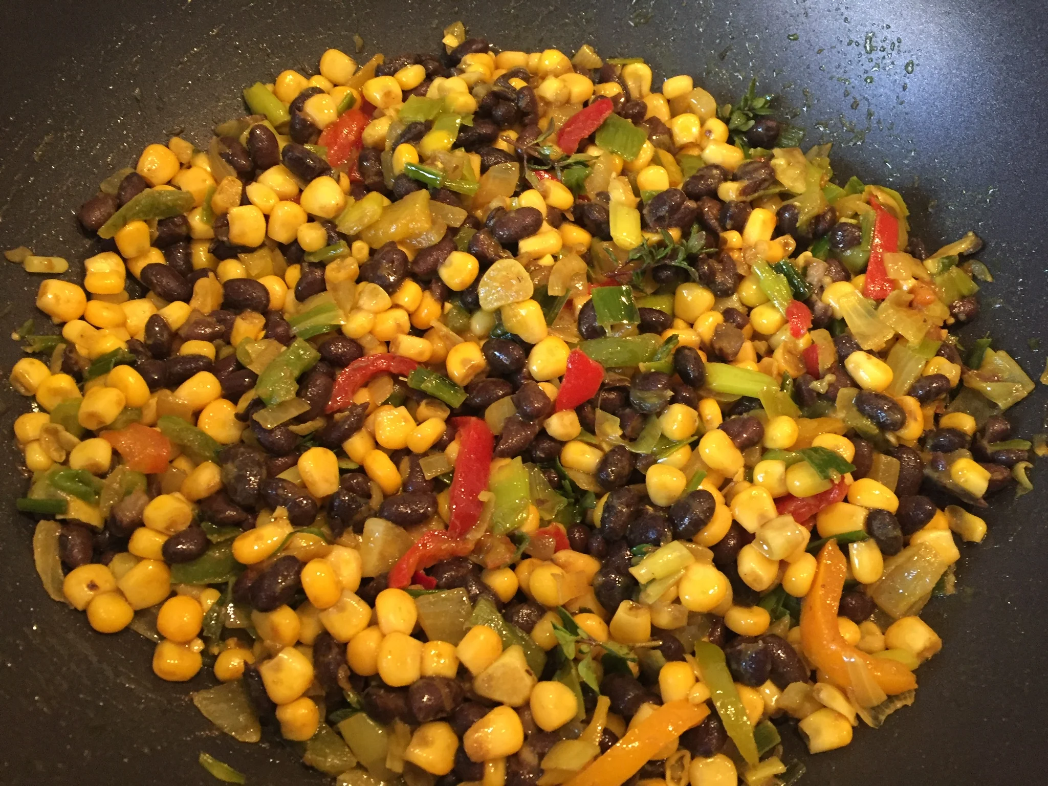 Steaming wok brimming with vibrant Cherokee-style succotash: golden corn kernels, black beans, red, green, yellow bell peppers, onions, and herbs.