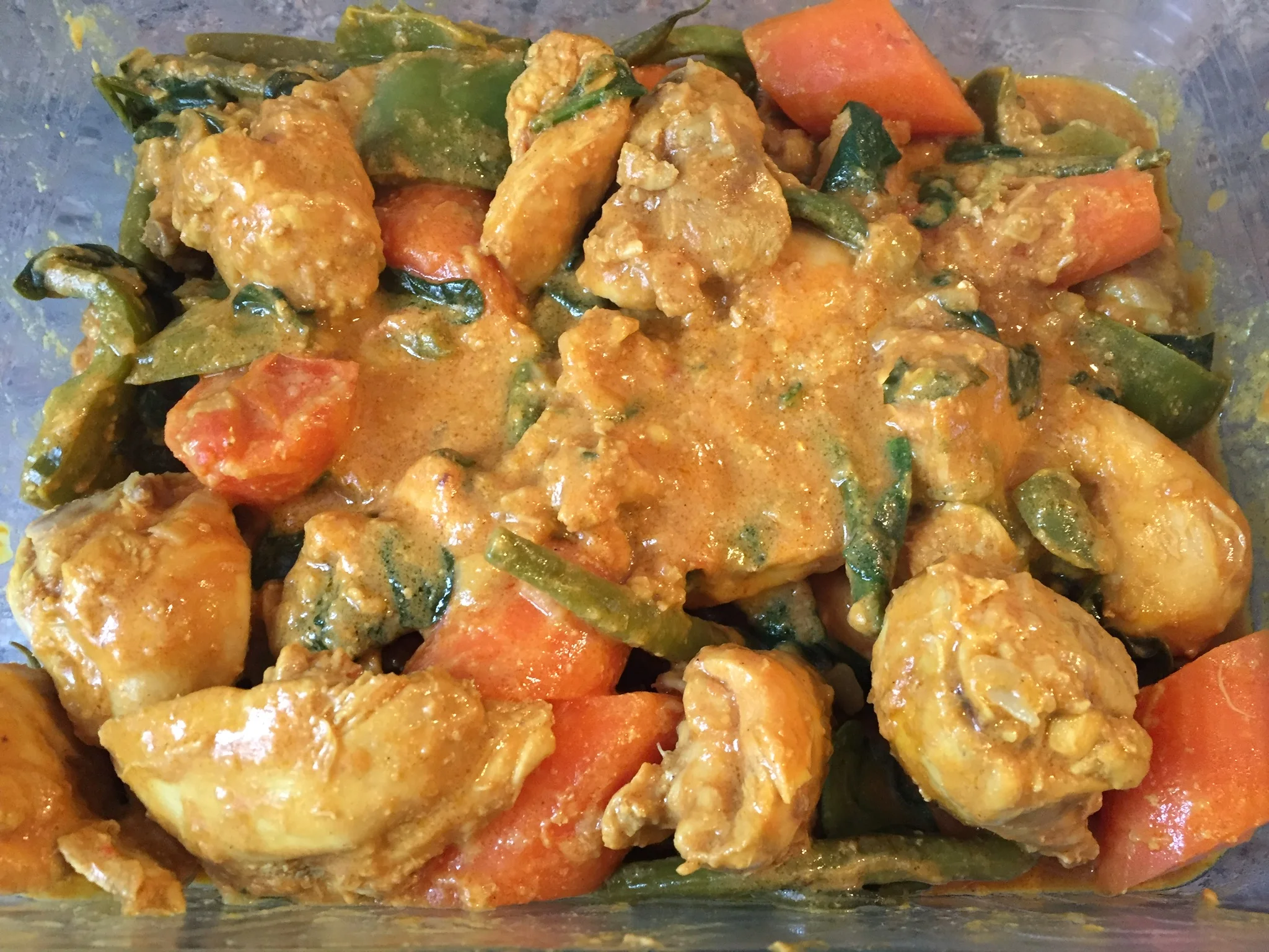 Tender chicken chunks in thick golden peanut sauce with orange carrots, green bell peppers, beans, and sweet potato chunks in a clear plastic container, vibrant and appetizing.